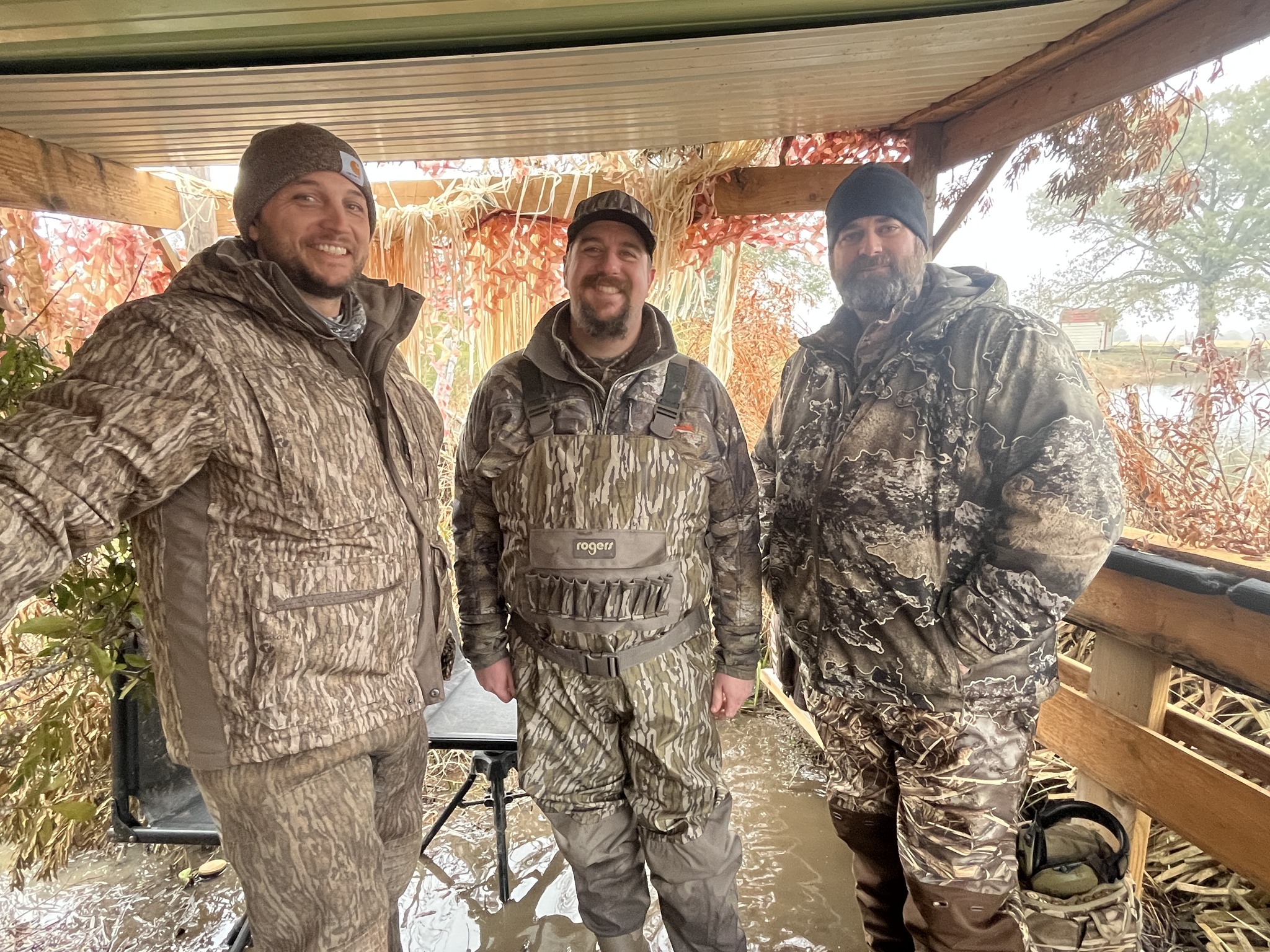 Three veterans smiling together at a duck blind after a morning hunt